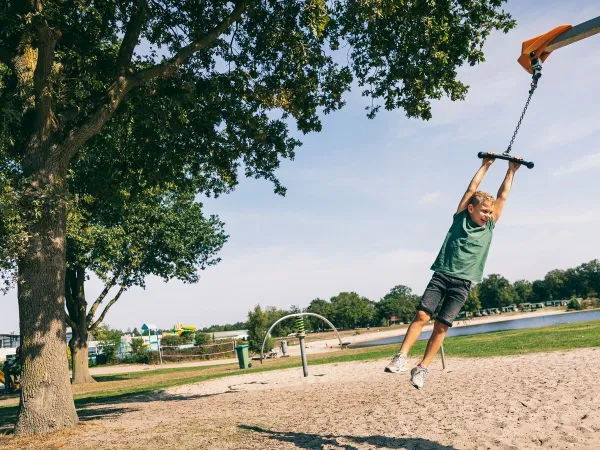 Kind, das auf dem Spielplatz des Campingplatzes Roan de Schatberg am Seil schaukelt.