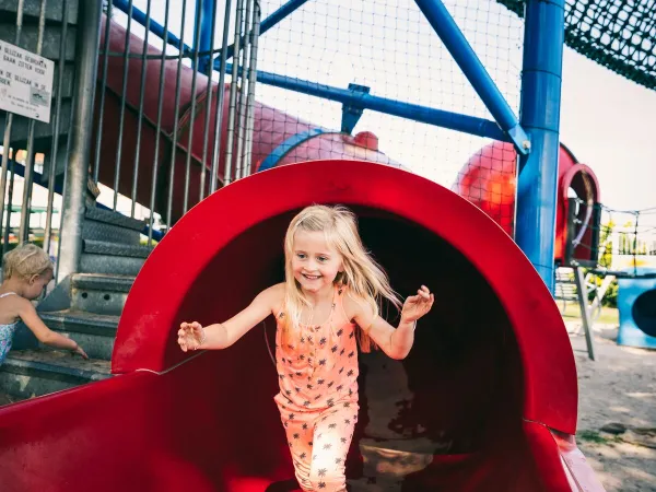 Ein Kind rutscht die Rutsche auf dem Spielplatz des Roan Luxury Camping De Schatberg hinunter.