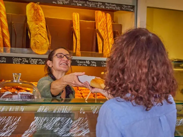 Eine Frau holt Baguettes aus der Bäckerei auf dem Roan Campingplatz Les Dunes.