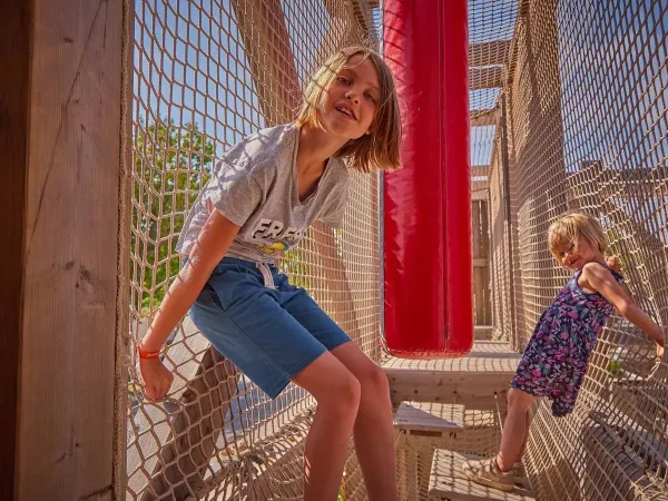 Spielende und kletternde Kinder im Klettergerüst auf dem Roan Campingplatz Le Petit Mousse.
